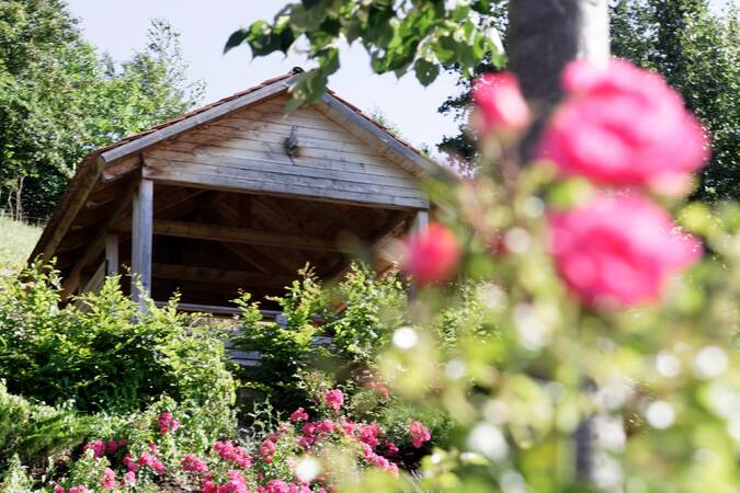 Ein Holzpavillon steht in einem grünen Garten, umgeben von blühenden Rosenbüschen.