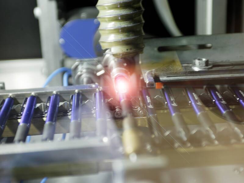 Eine Produktionsmaschine graviert mit einem Laser Texte auf eine Reihe von Kugelschreibern.