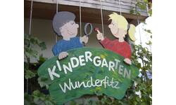 Ein farbenfrohes Schild mit zwei stilisierten Kindern zeigt den Namen "Kindergarten Wunderfitz".